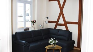 Un sofá seccional azul oscuro con una pequeña mesa redonda de madera frente a él, una alfombra gris y una pared de madera con un diseño geométrico.