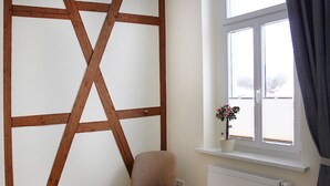 Una habitación con pared de vigas de madera, una silla, una ventana con una planta y un radiador.