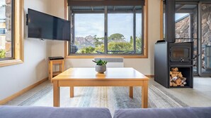 Ein modernes Wohnzimmer mit großem Fenster, einem Flachbildfernseher, einem Holztisch und einem Steinkamin.