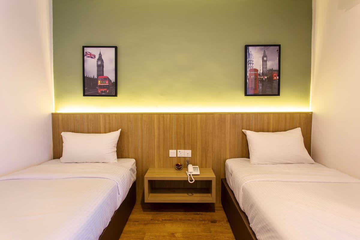 Habitación de hotel con dos camas, cabecera de madera, mesita de noche con teléfono y dos cuadros con imágenes de lugares emblemáticos de Londres.