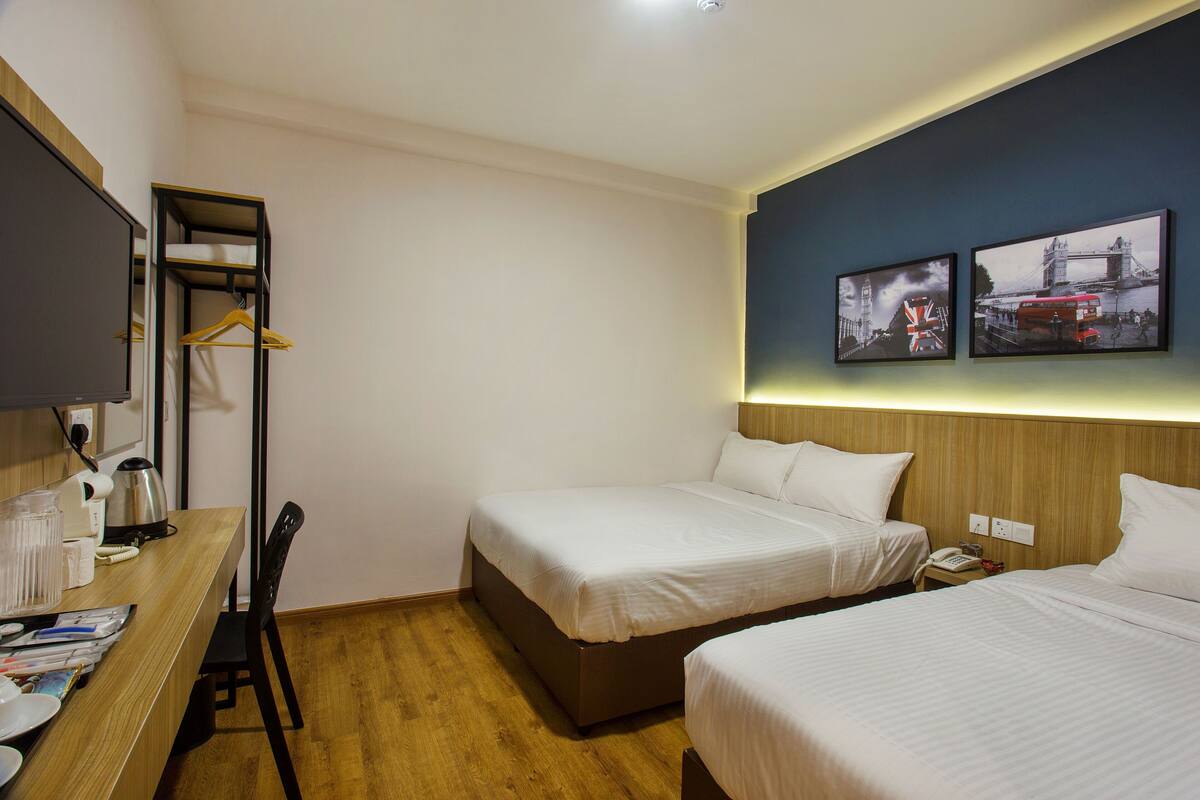 Habitación de hotel con dos camas, un escritorio con una silla, una cafetera y un armario con ropa colgada.