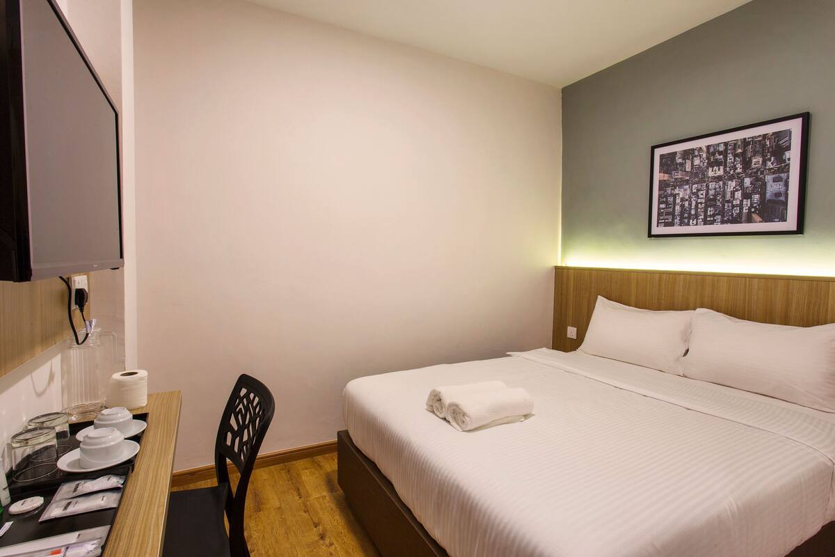 Un cuarto de hotel con una cama bien hecha, un escritorio con una silla y un cuadro en la pared.