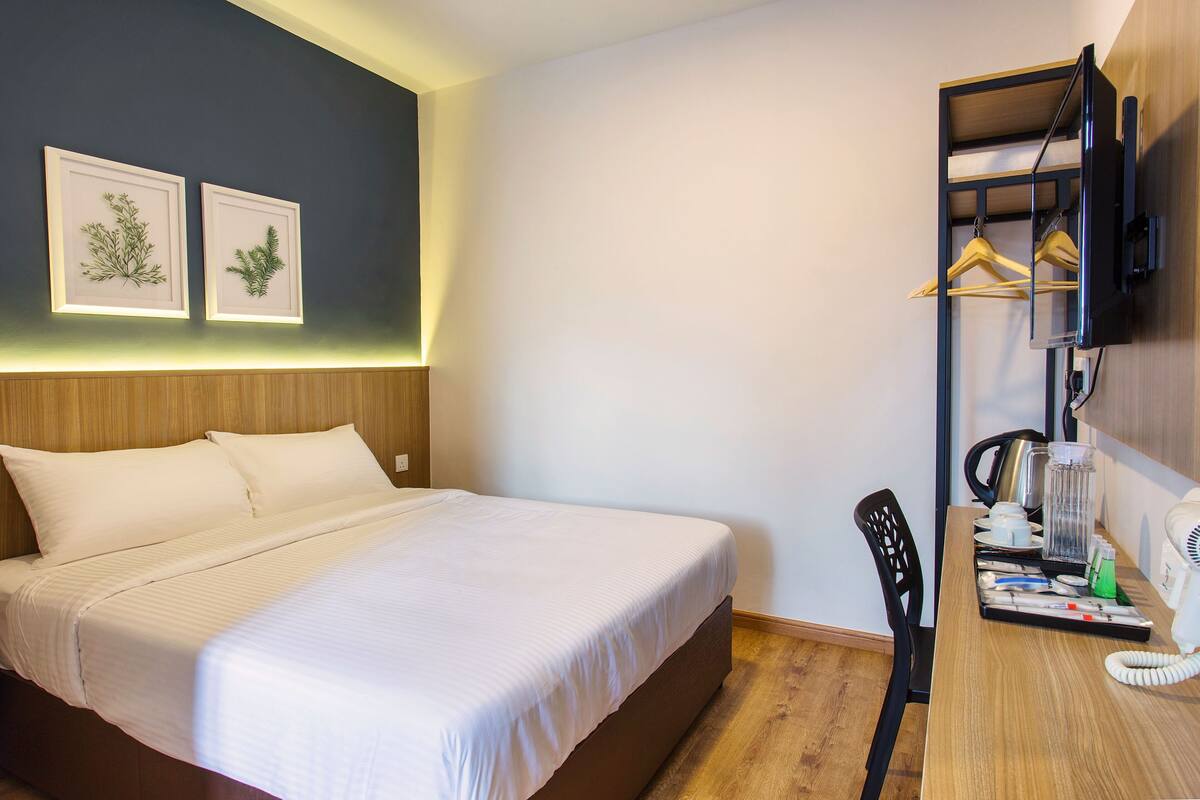 Una habitación de hotel con cama, escritorio, teléfono, cafetera y televisor en la pared.