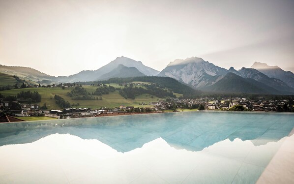 A mountain town with a reflective pool, houses, and a church. - Excelsior Dolomites Life Resort (Marebbe)