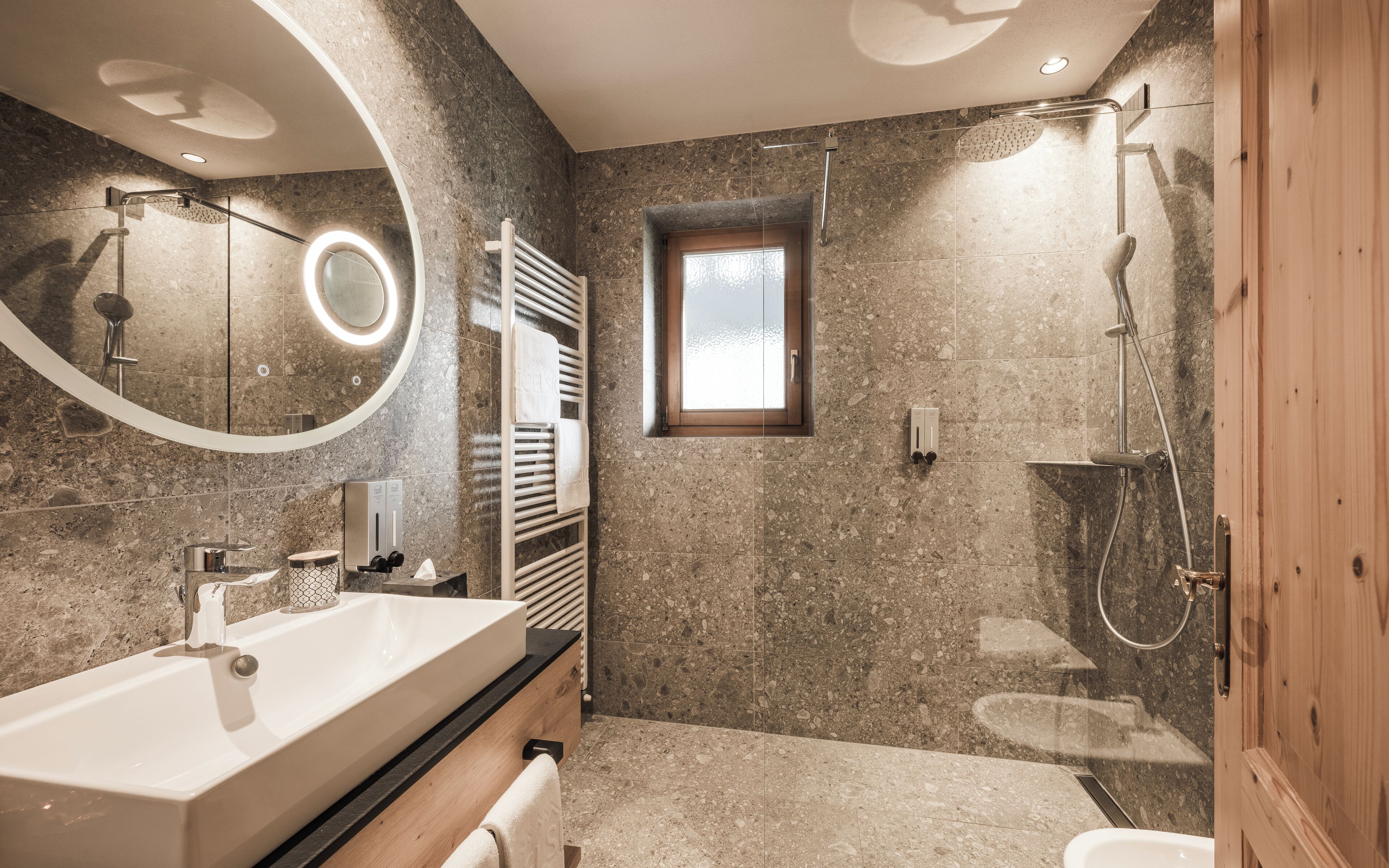 A modern bathroom with a large sink, a mirror, a shower, and a small window.