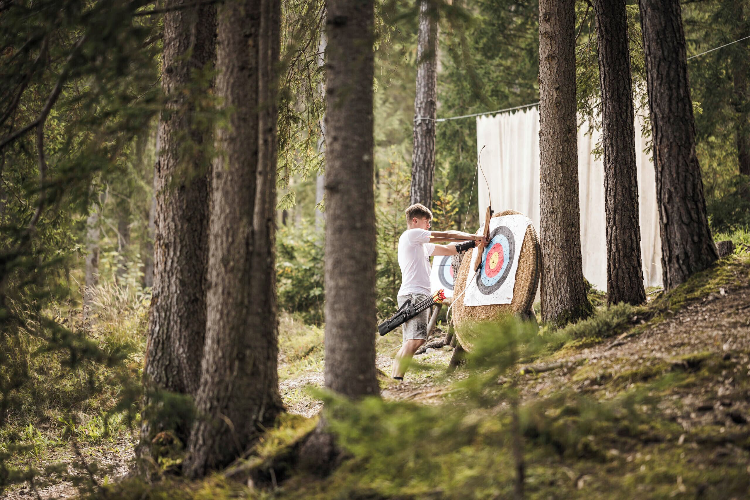A person aiming an arrow at a target in a forested area.