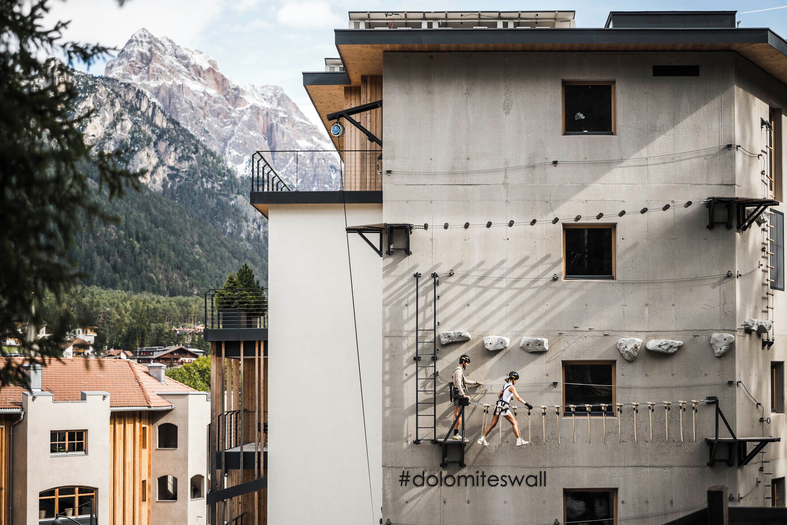 Un edificio con un mural #dolomiteswall, un balcón y montañas al fondo.