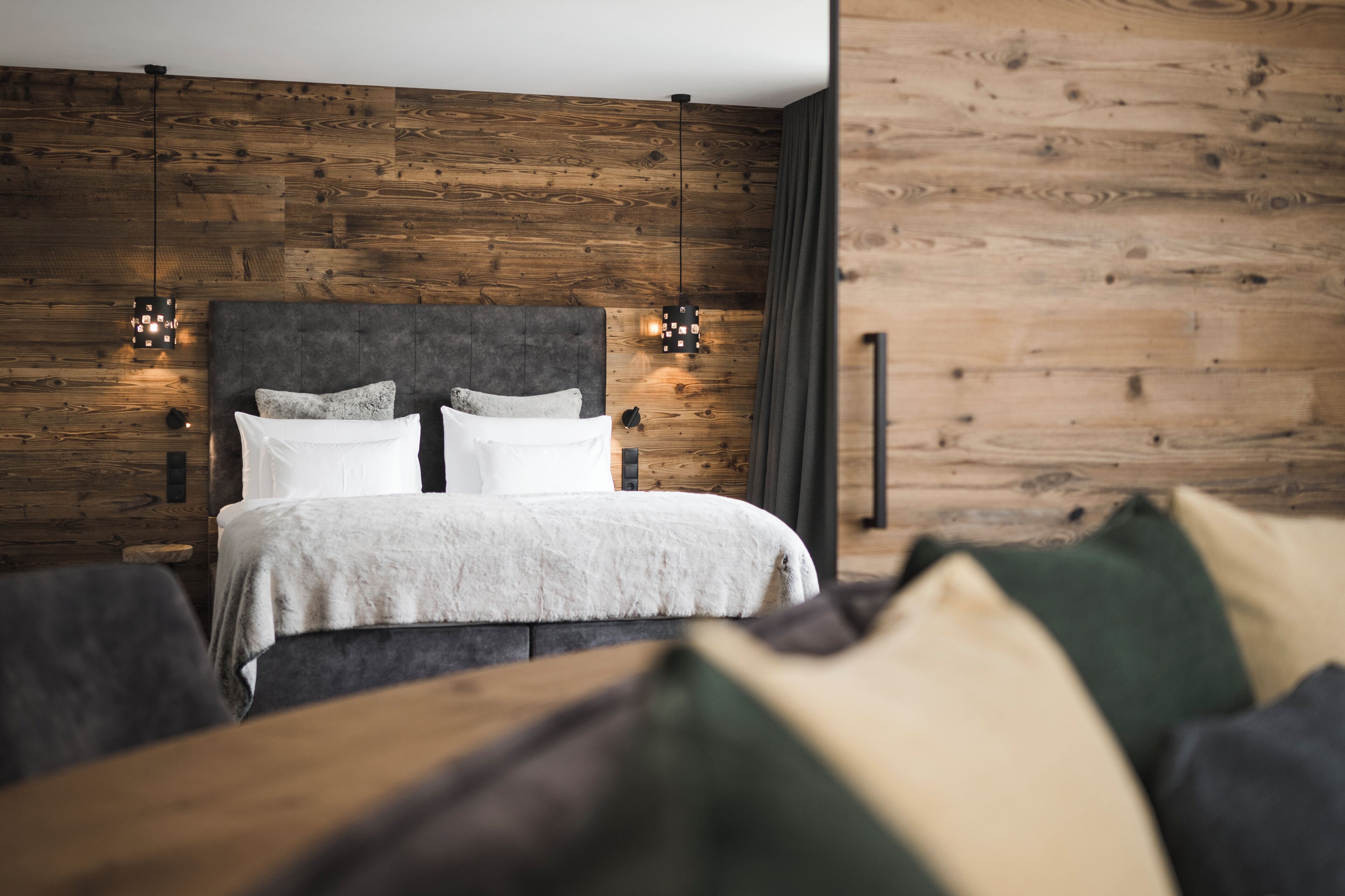 Een moderne slaapkamer met een houten wandpaneel, een groot bed met wit beddengoed en twee hanglampen.