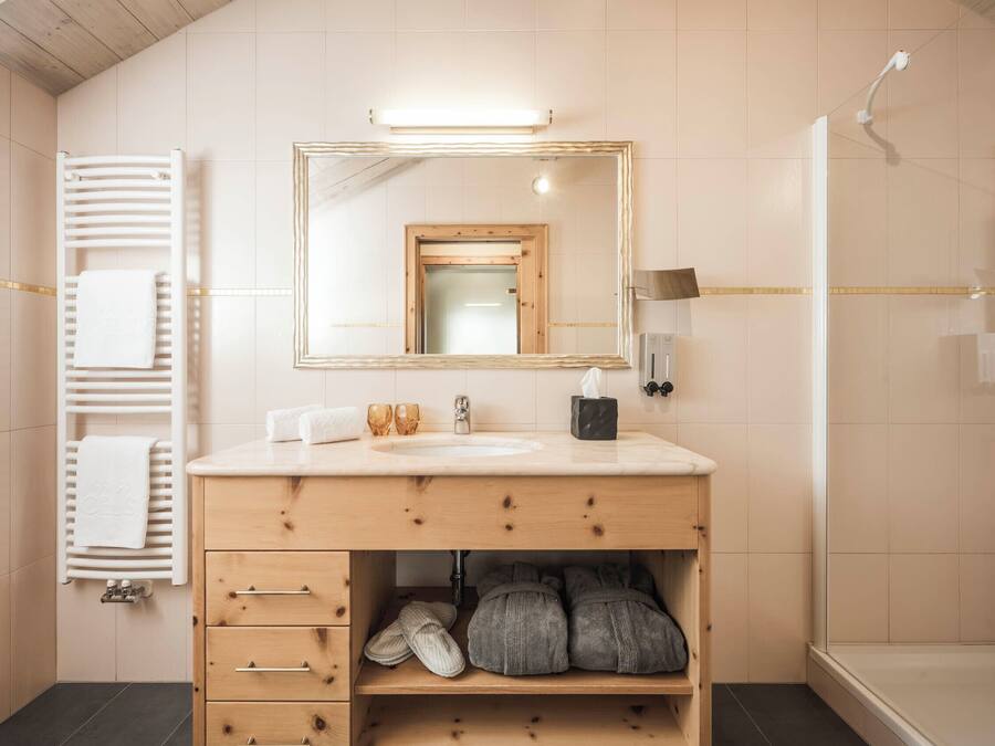 Een moderne badkamer met een houten wastafelmeubel, een grote spiegel, een handdoekhouder en een douchehoek.