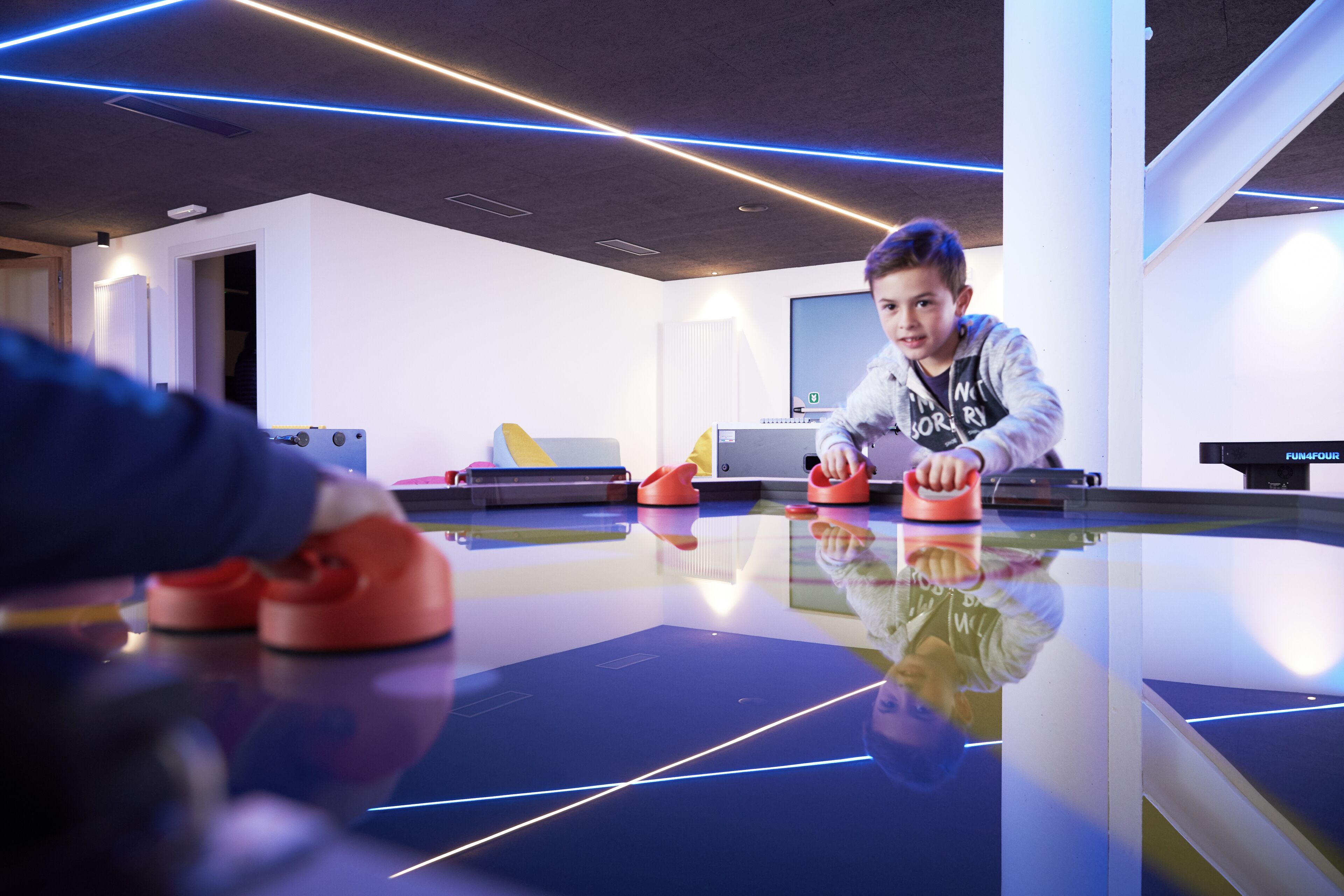 Een moderne kamer met een glazen tafel, een persoon die een spelletje speelt, en een groot scherm op de achtergrond.