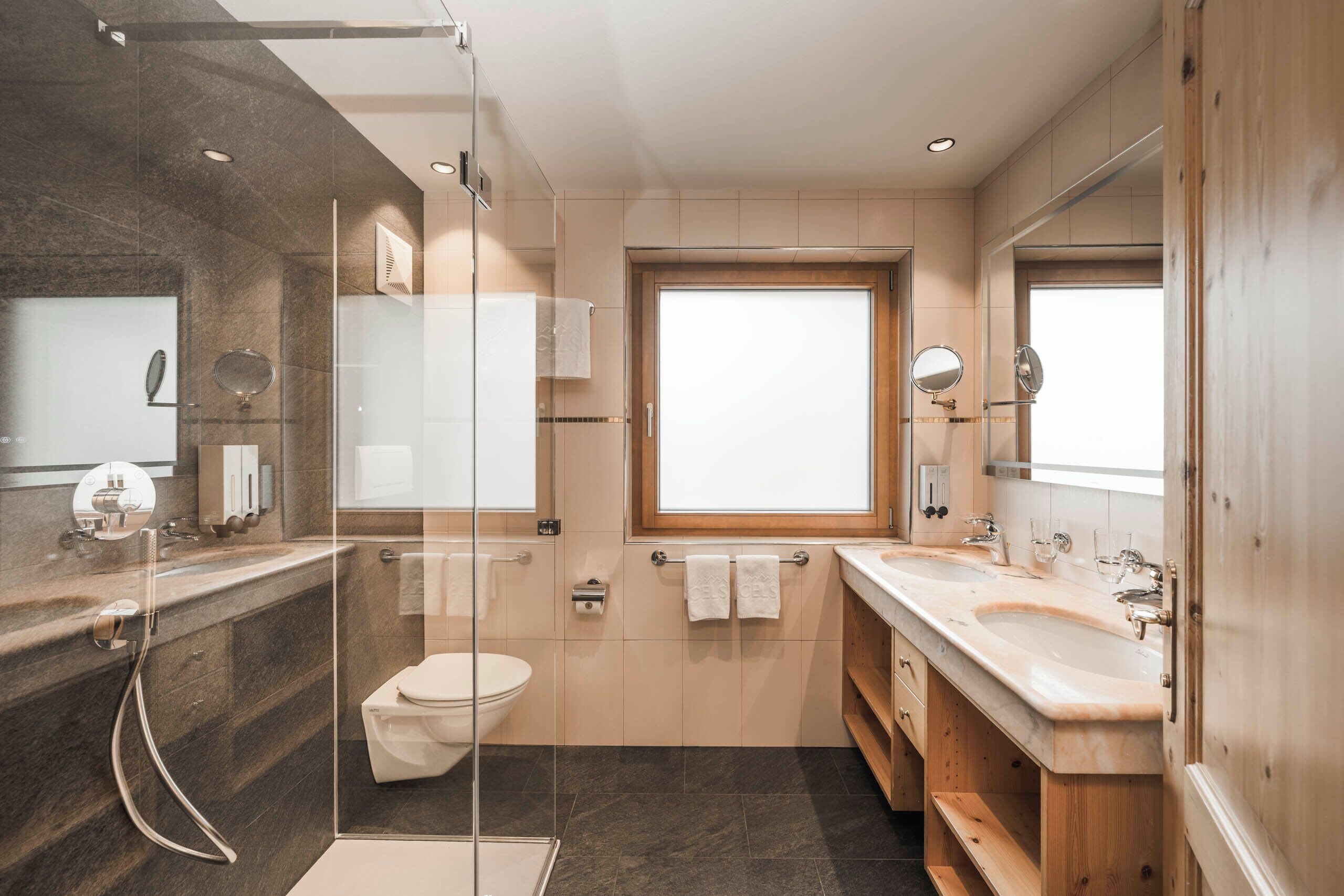 A modern bathroom with a glass-enclosed shower, a large window, and a wooden vanity with a sink and mirror.