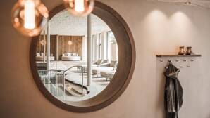 A modern interior with a round mirror reflecting a lounge area, a staircase, and a coat rack.