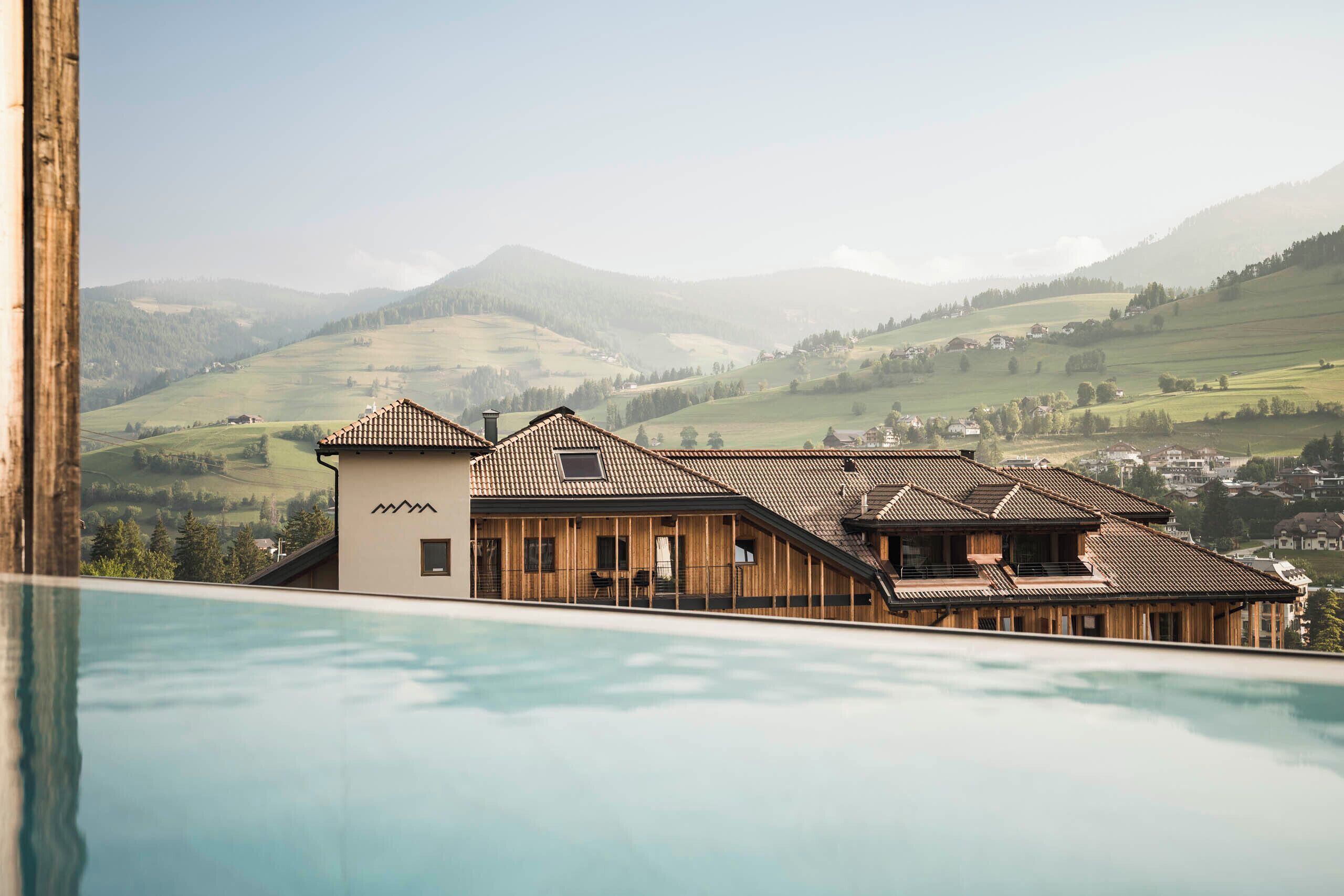 A modern building with a swimming pool, wooden exterior, and a view of rolling hills.
