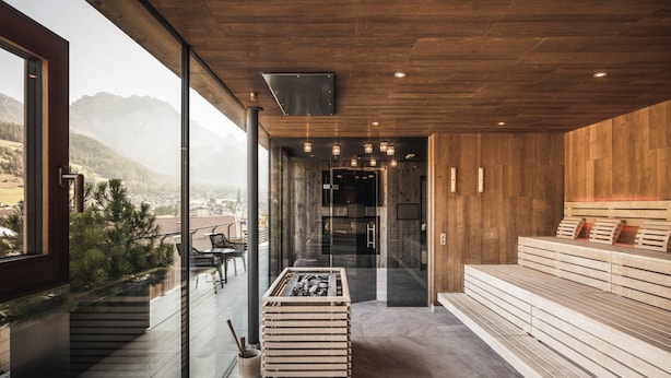 A modern interior with a wooden ceiling, a glass wall offering a mountain view, a seating area with wooden benches, and a fireplace.