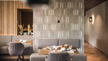 A modern dining area with a wooden wall, grey cushioned seating, and a table set with breakfast.