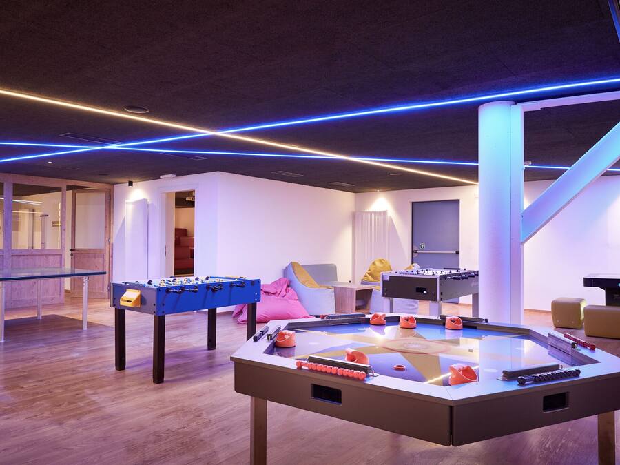 Un espacio interior moderno con mesa de fútbol de mesa, mesa de ping pong y una mesa de fútbol de mesa con diseño azul y naranja.