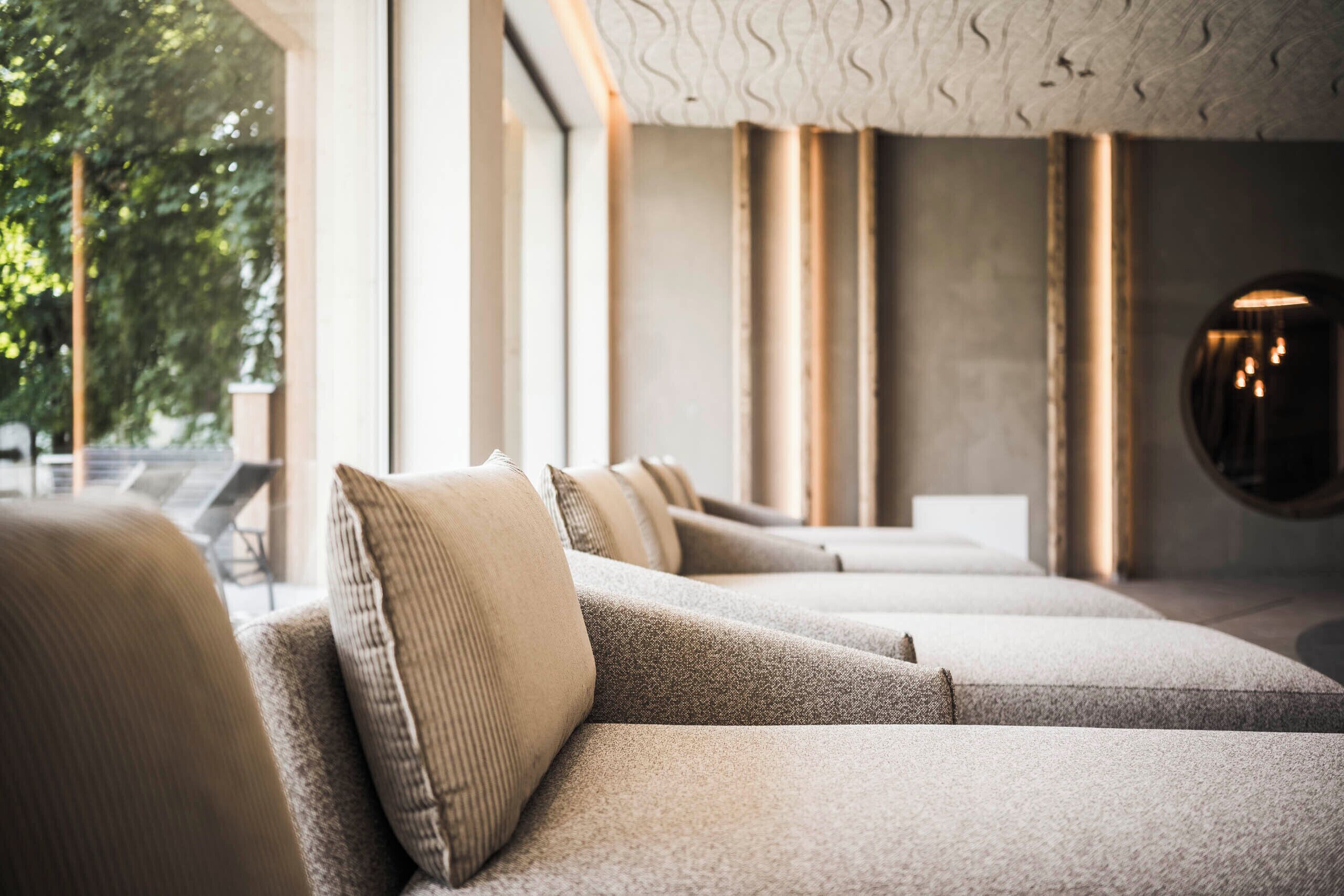 A modern interior with a sofa and cushions, a patterned ceiling, and a round wall light.