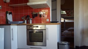 A kitchen with a stainless steel oven, white cabinets, and a red tiled backsplash. - Original round wood house T3 sea view (Locquirec)
