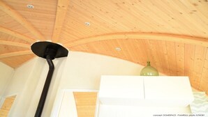 A room with a wooden ceiling, a black pipe, a white air conditioning unit, and a green bottle on a shelf. - Original round wood house T3 sea view (Locquirec)