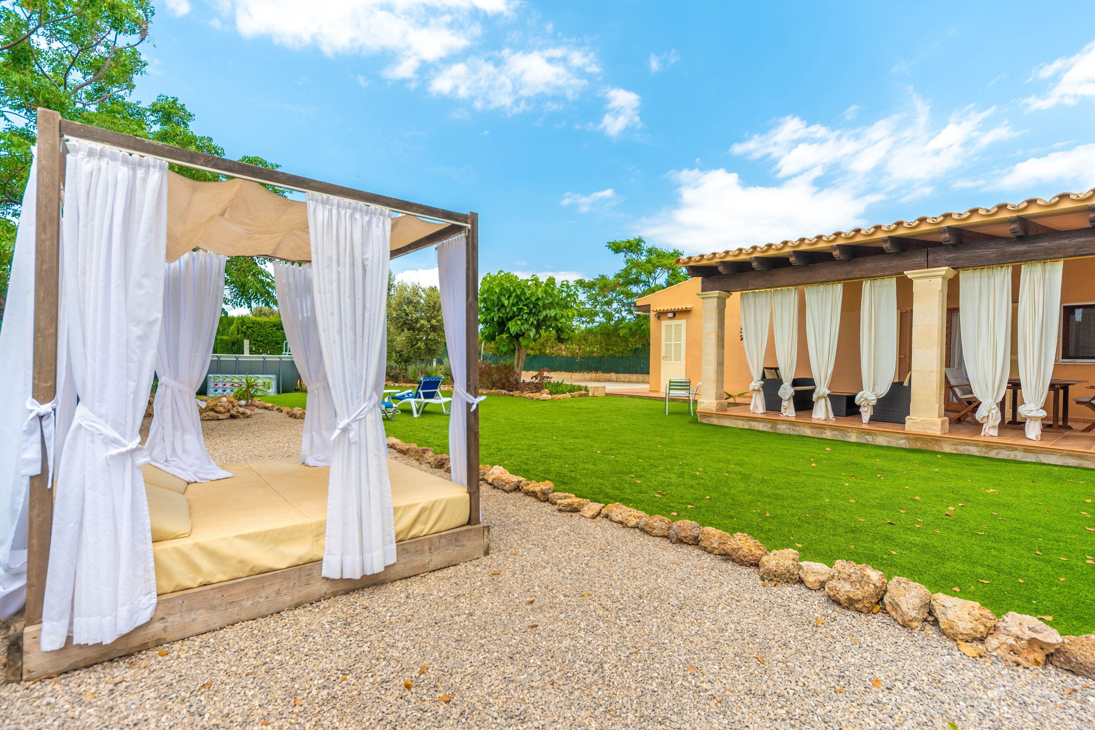 A gazebo with white curtains, a grassy lawn, and a building with multiple rooms.