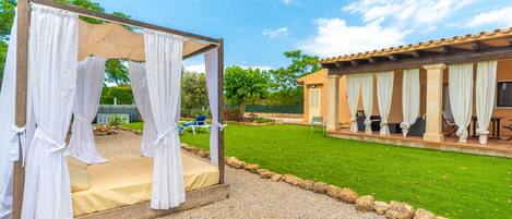 A gazebo with white curtains, a grassy lawn, and a building with multiple rooms.