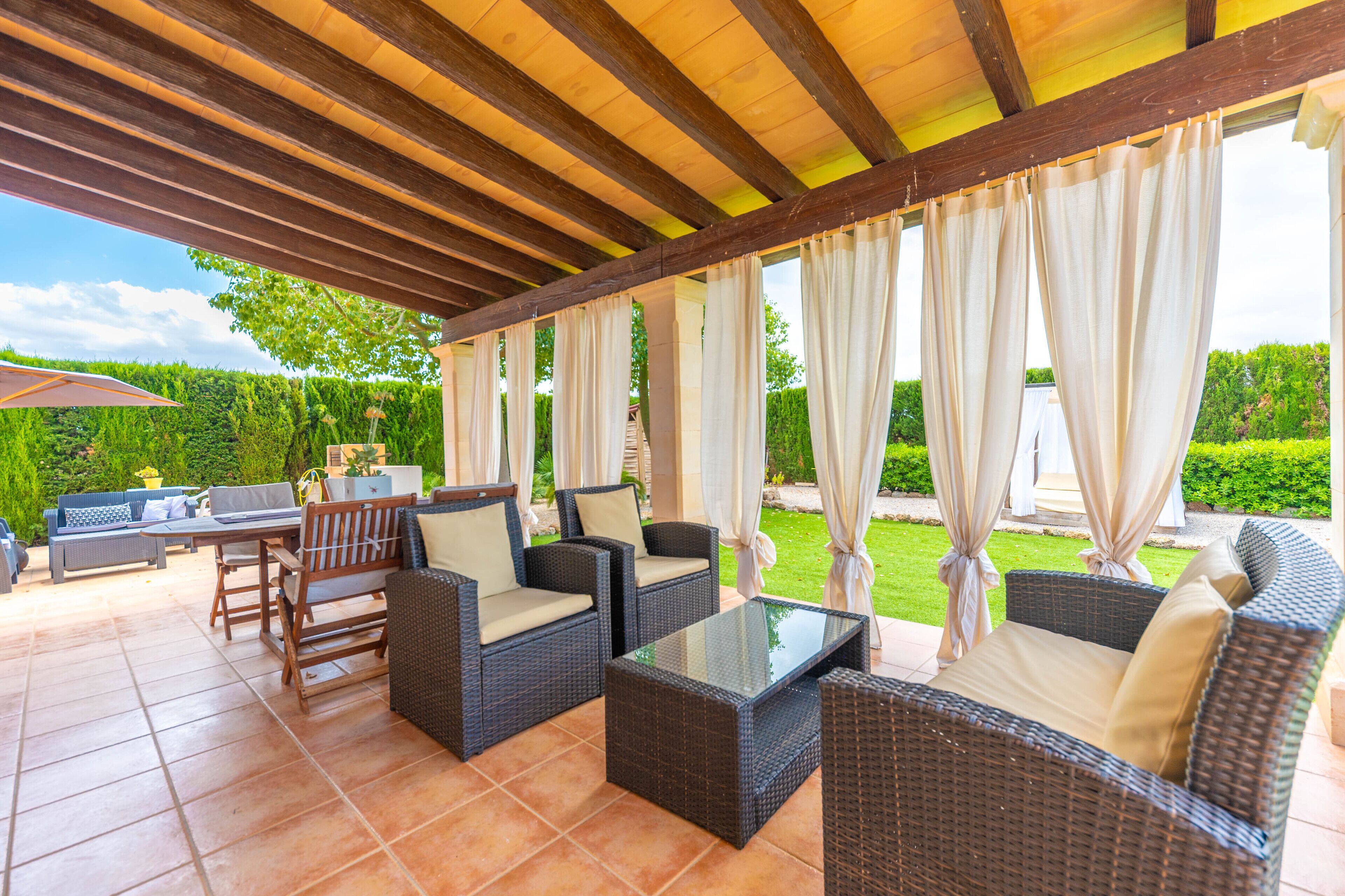 Eine Terrasse im Freien mit Korbmöbeln, einem Tisch mit Glasplatte und Blick auf einen gepflegten Garten.