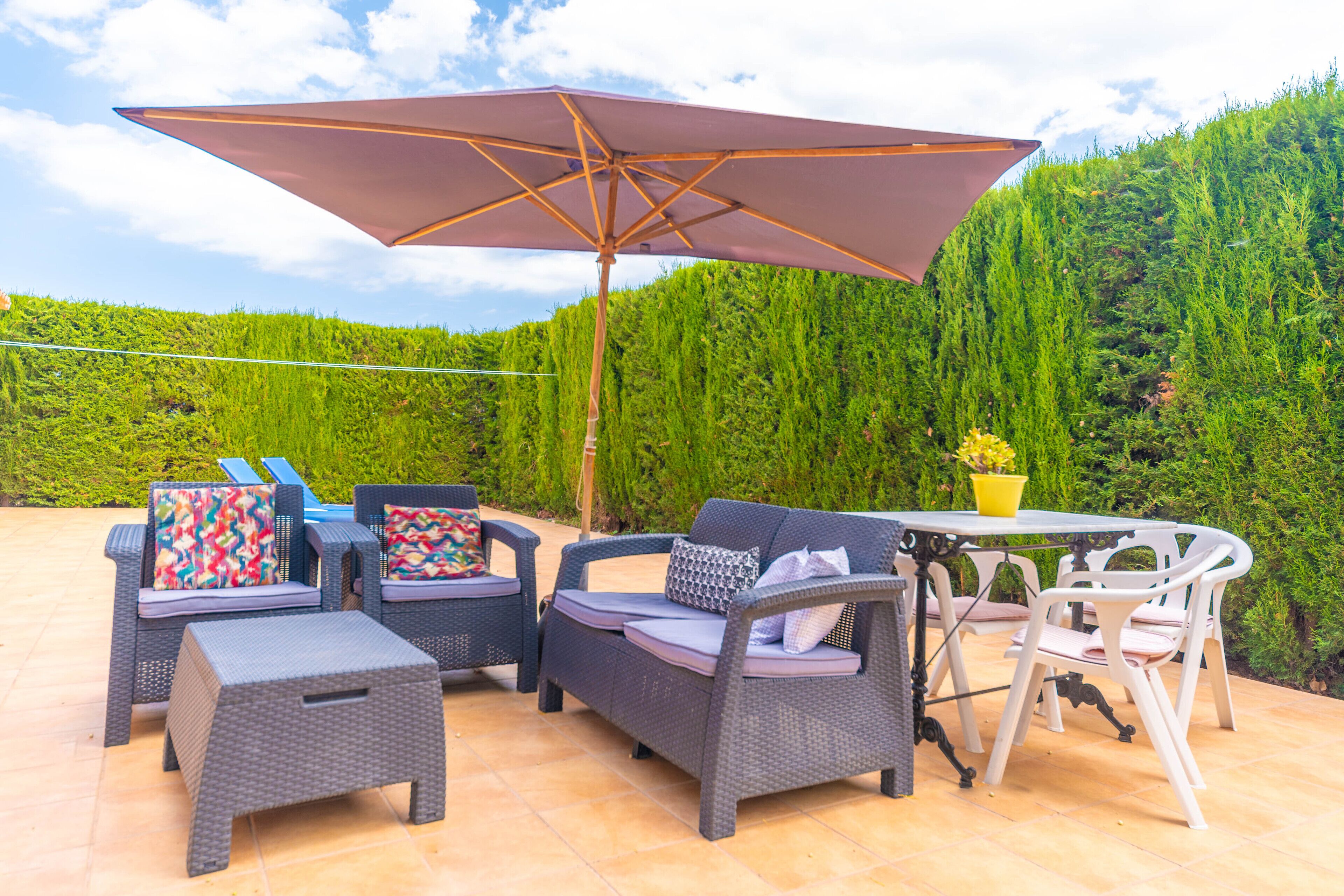 Eine Terrasse im Freien mit Korbmöbeln, darunter Stühle, eine Couch, ein Tisch und ein großer Sonnenschirm.