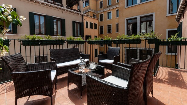 An outdoor patio with wicker furniture and a table, surrounded by buildings with balconies and windows. - San Marco Luxury property with terraces. Muneghe (Venezia)