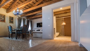 A spacious room with exposed wooden beams, a dining area with chairs and a table, and a modern bathroom with a glass shower. - San Marco Luxury property with terraces. Muneghe (Venezia)