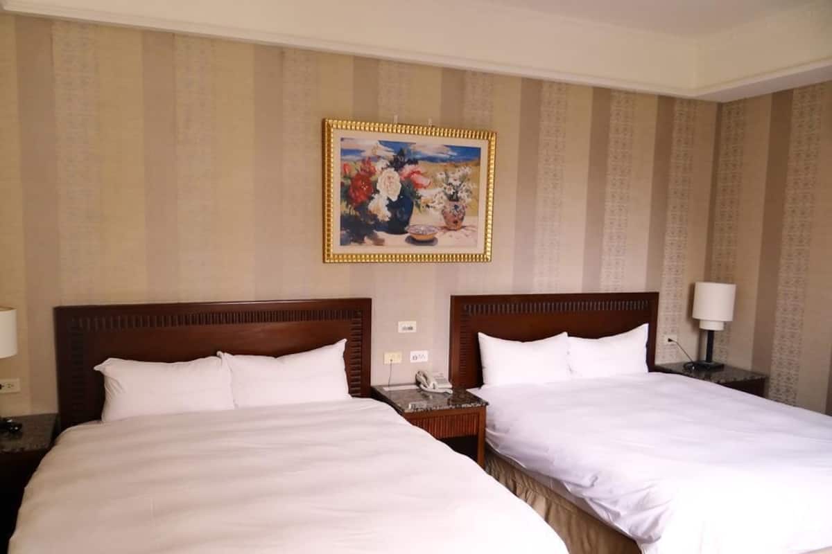 A hotel room with two beds, a painting on the wall, and a nightstand with a lamp.