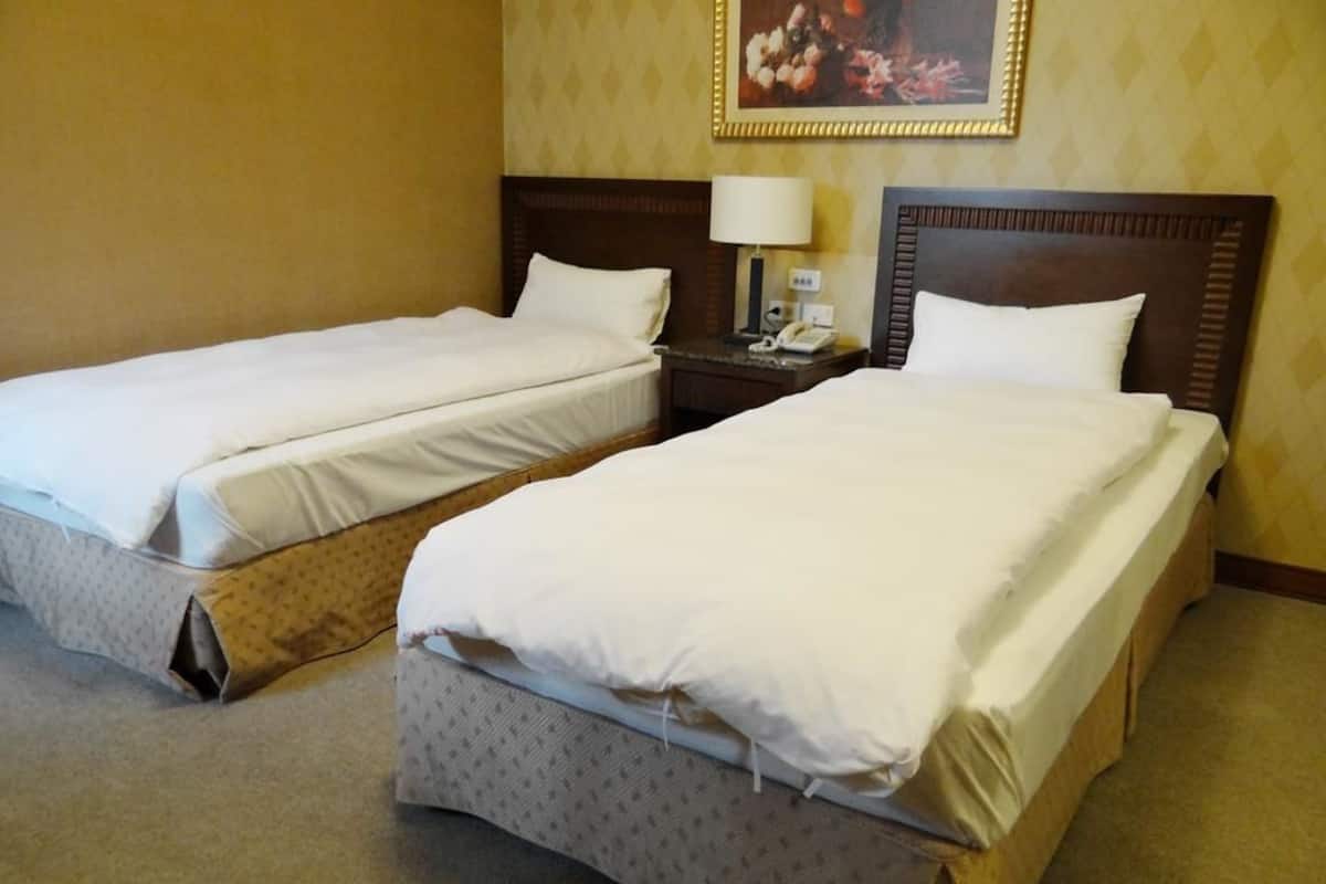 A hotel room with two single beds, a nightstand with a lamp, and a painting on the wall.
