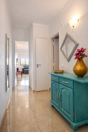 A hallway with a teal cabinet, a gold vase with flowers, and a mirror on the wall.