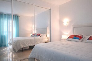 A hotel room with two beds, a large mirror, and a view of the sea.