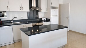 Una cocina moderna con armarios blancos, una isla con cubierta negra, electrodomésticos de acero inoxidable y un microondas.