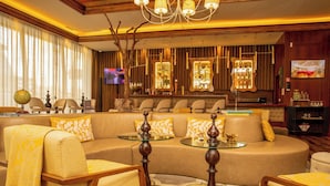 A luxurious living room with a curved sofa, armchairs, a glass coffee table, and a bar area with a television and bar stools.