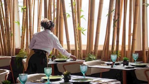 A restaurant with bamboo partitions, tables set with green plates, and blue glassware.