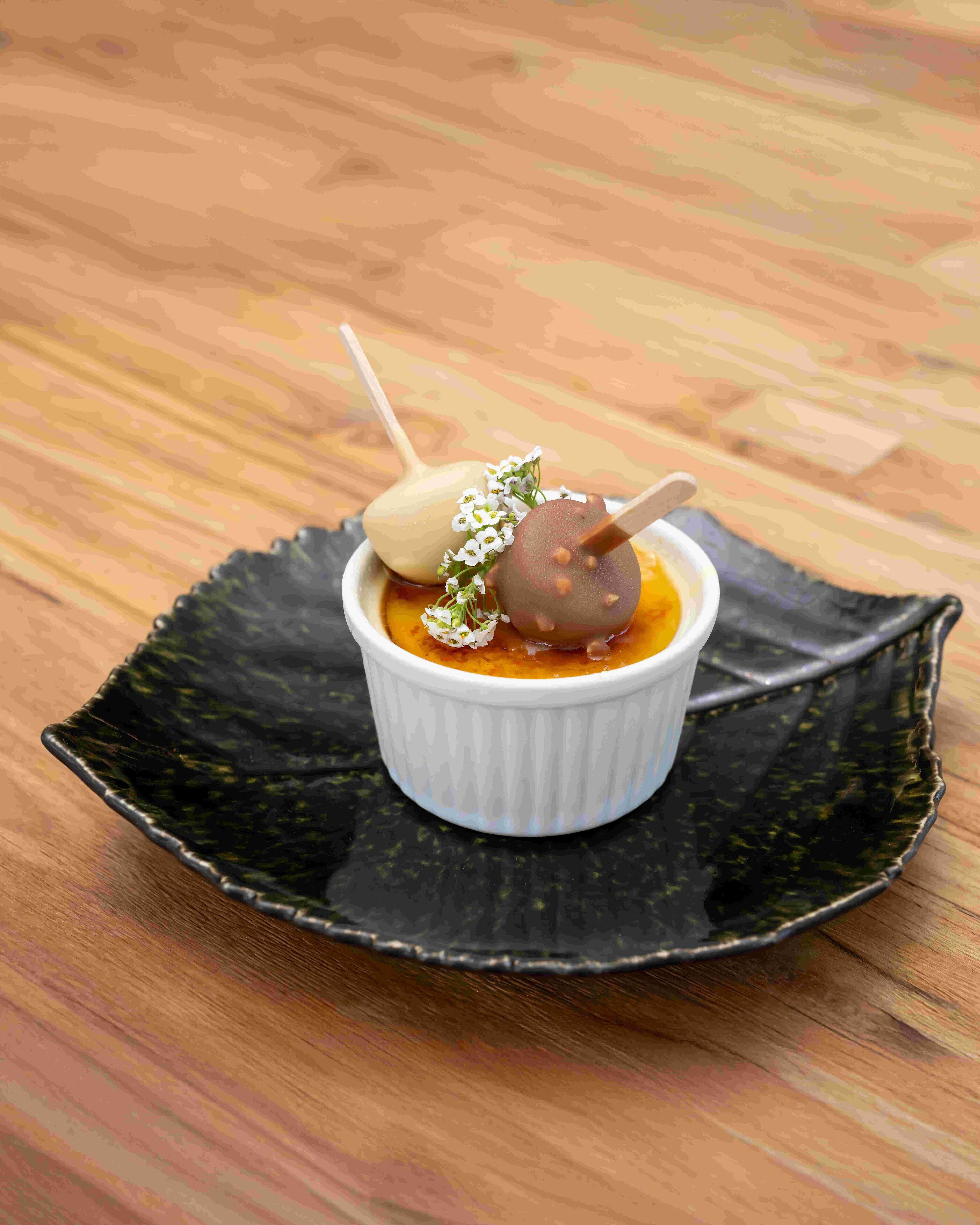 A dessert in a white ramekin on a black plate.