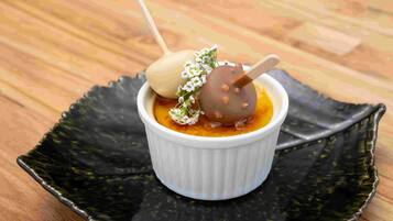 Un postre en un recipiente blanco sobre un plato negro.