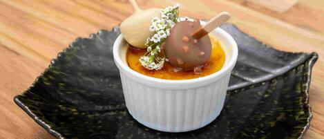 A dessert in a white ramekin on a black plate.