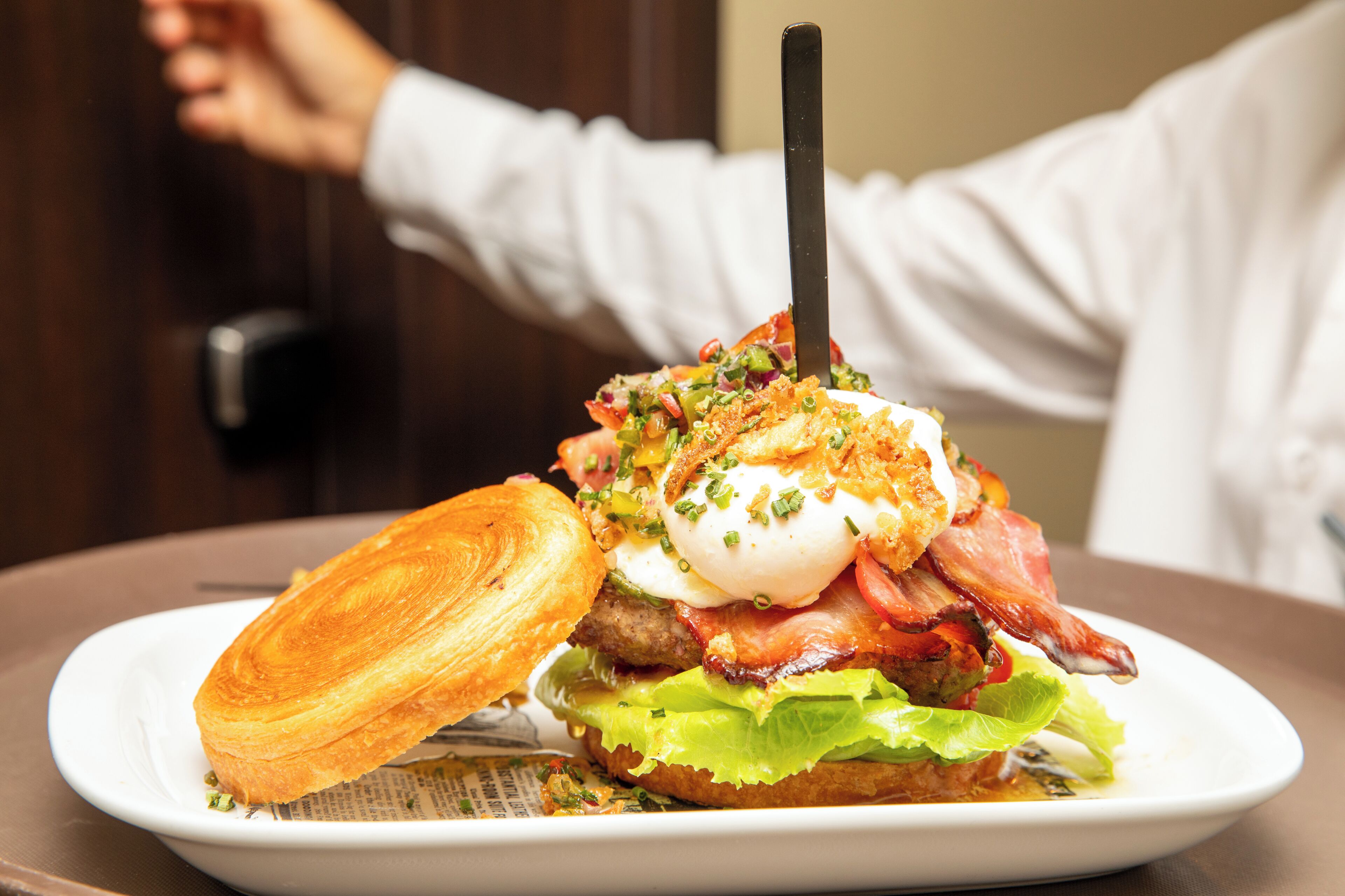 Un sándwich de desayuno con tocino, huevo y lechuga sobre un plato blanco.