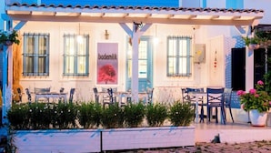 A two-story building with a blue facade and pink shutters, featuring outdoor seating and a sign that reads "bademlik". - Bademlik Otel (Bozcaada)