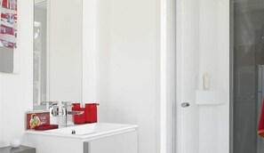 A modern bathroom with a white sink, red soap dispensers, and a glass shower enclosure.