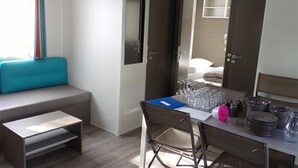 A room with a dining table set for two, a sofa, and a mirror. - Camping La Cailletiere - Mobil-Home (Dolus-d'Oleron)
