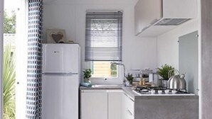 A compact kitchen with a refrigerator, sink, stove, and window with blinds. - Camping La Cailletiere - Mobil-Home (Dolus-d'Oleron)