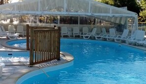 Piscina con cerramiento de madera, sillas de descanso blancas y un área cubierta con toldo blanco.
