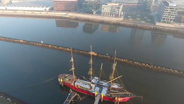 A large red ship docked at a pier with a cityscape in the background. - Klabauterbett (Bremen)