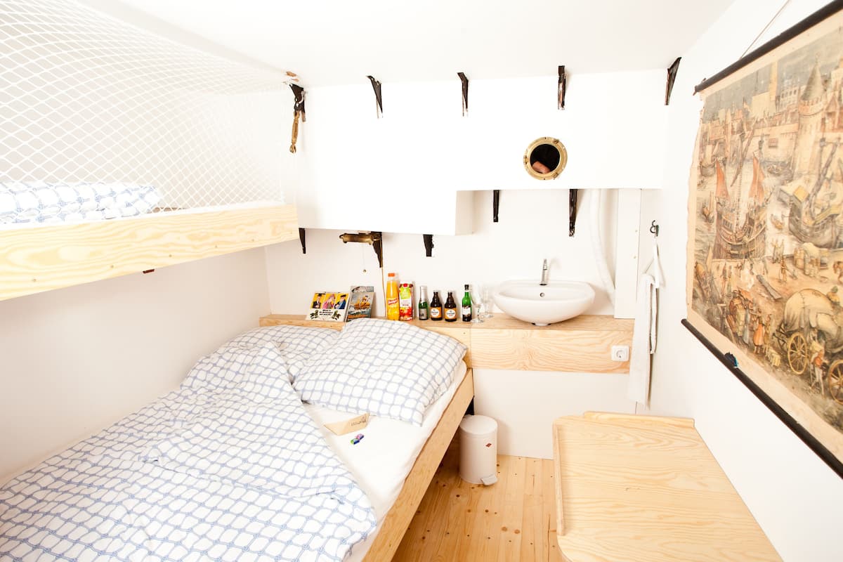 A small, neatly organized room with a bunk bed, a sink, and a painting on the wall.