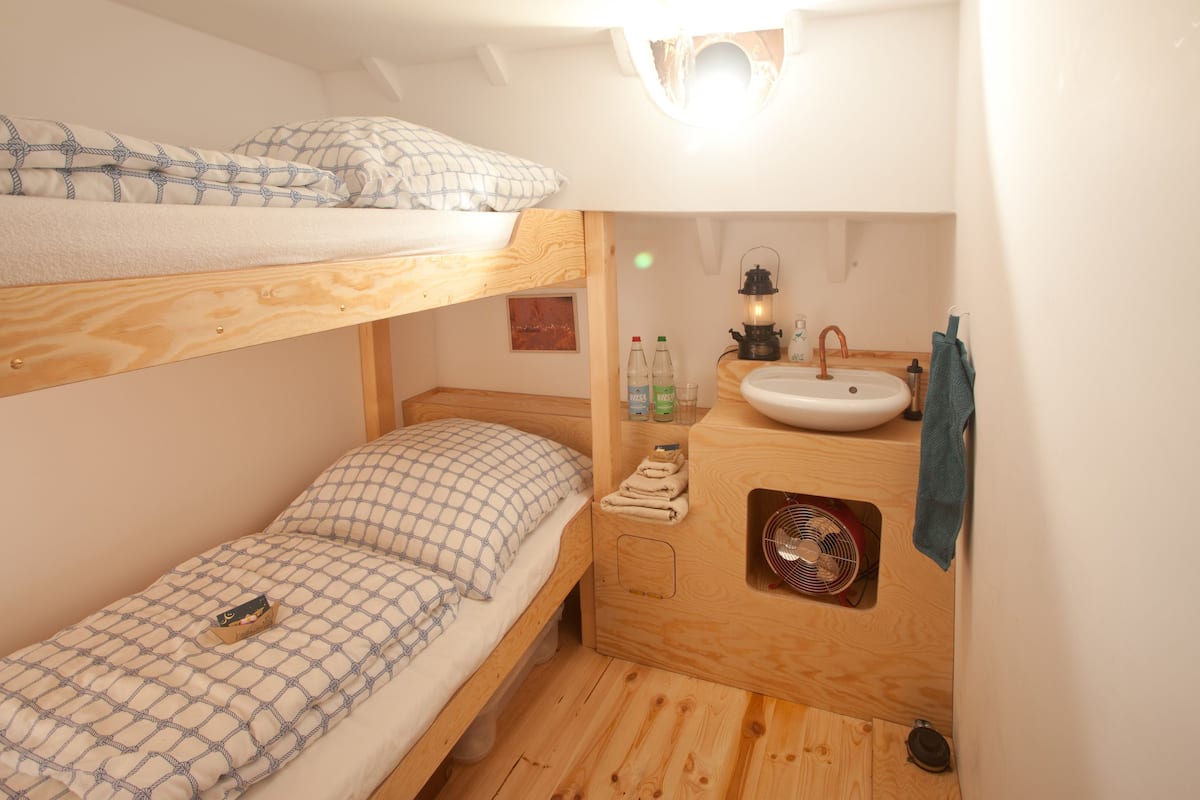 A compact room with a bunk bed, a small sink, and a fan.