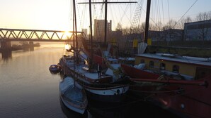 A harbor with several boats docked, a bridge in the background, and buildings along the shore. - Klabauterbett (Bremen)