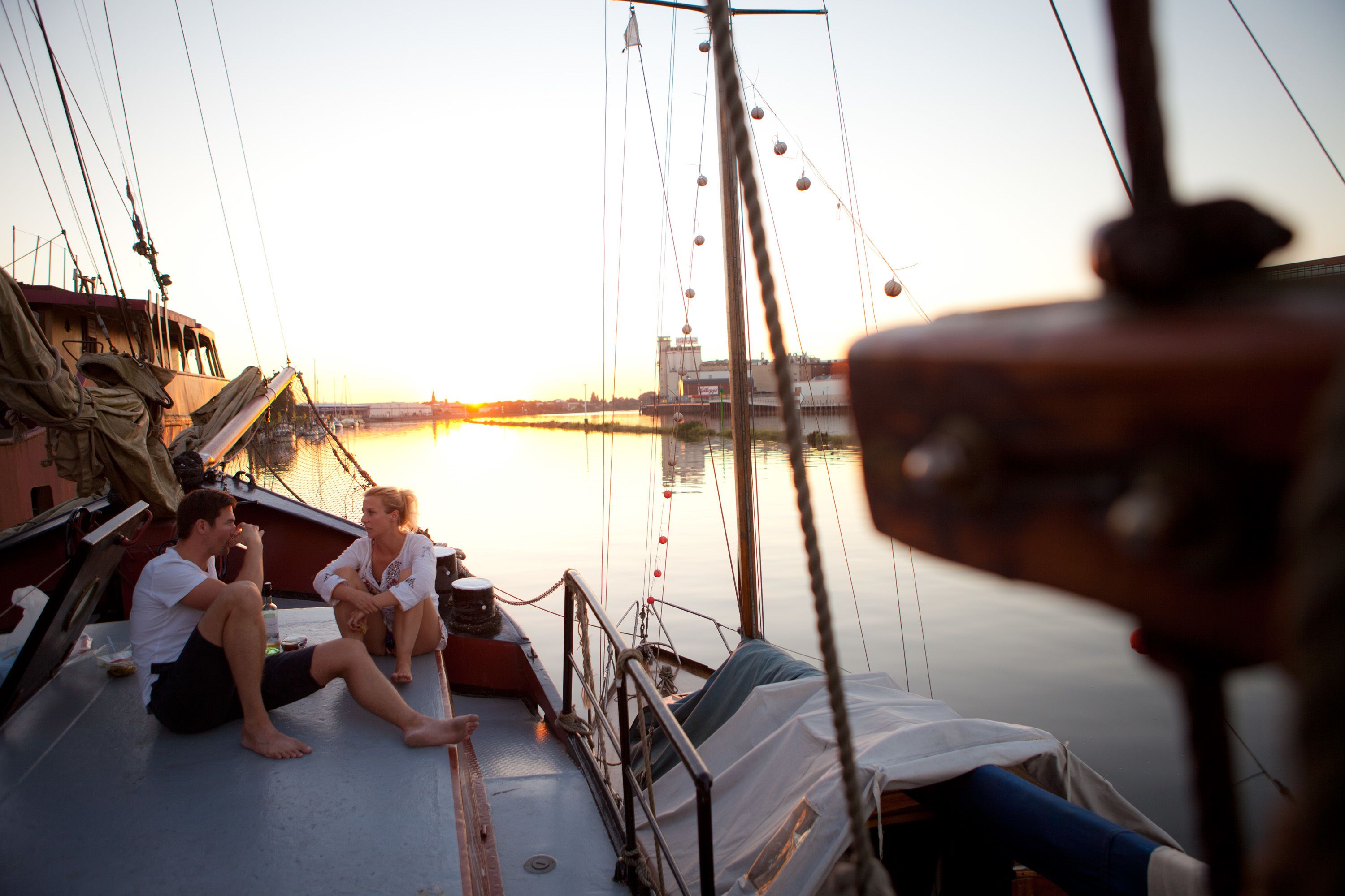Ein Boot mit zwei Personen, die auf dem Deck sitzen, einer Reling und Blick auf das Wasser.